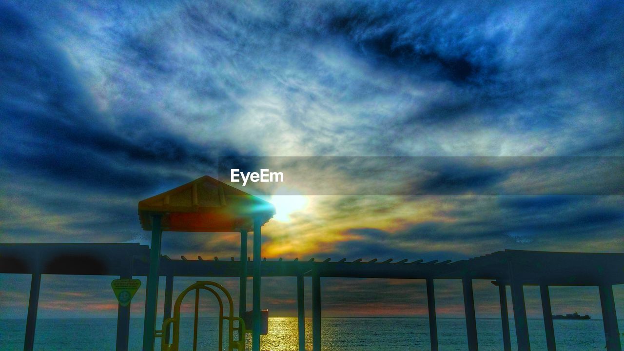 Low angle view of pier on sea against cloudy sky during sunset