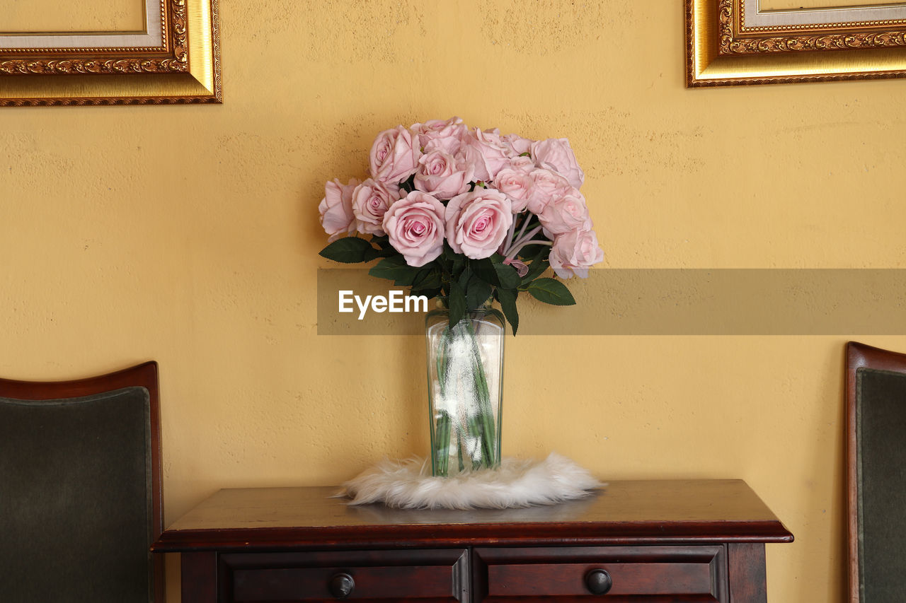 Some artificial rose flower in a vase on the wooden table in a vintage style coffee shop