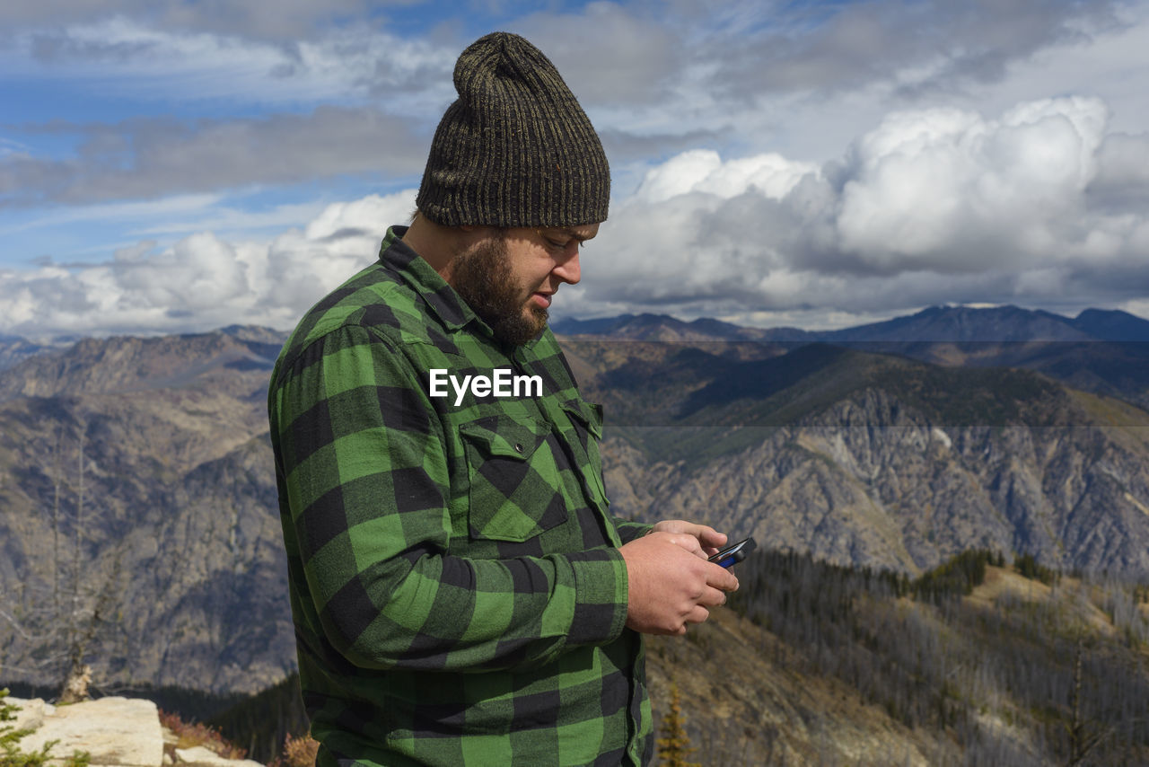 Male in flannel with cell phone on mountain top