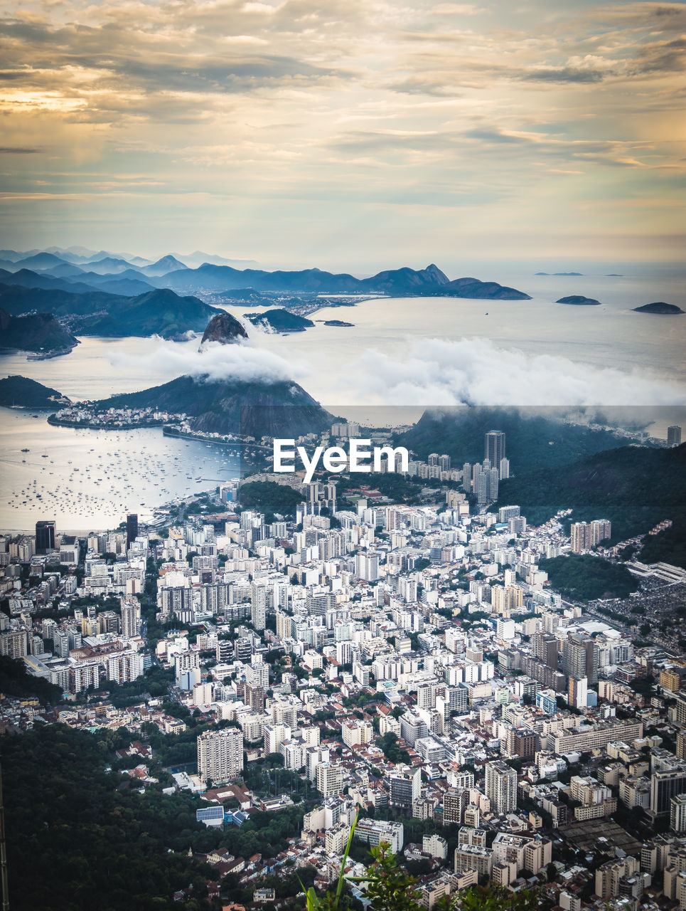 Aerial view of townscape by sea against cloudy sky during sunset