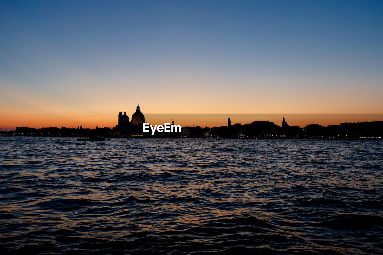 River by silhouette cityscape against sky during sunset