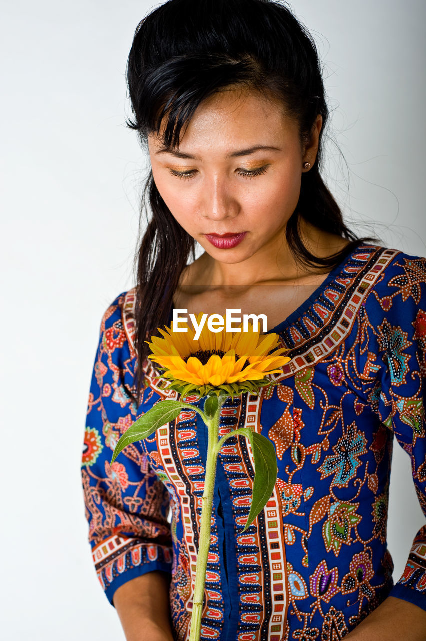 Woman looking at sunflower against white background