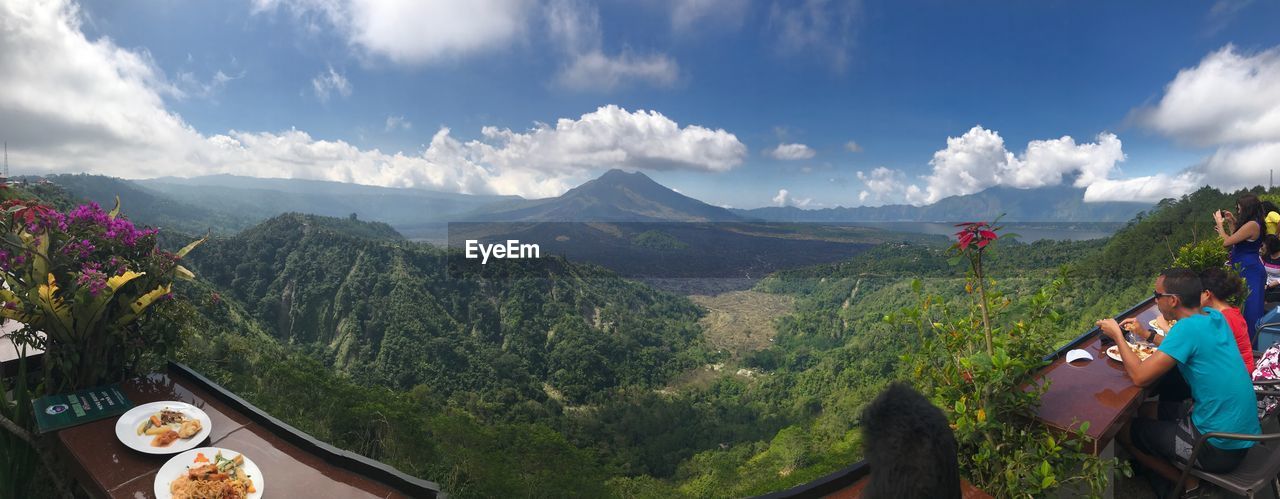 PANORAMIC VIEW OF PEOPLE SITTING AGAINST MOUNTAIN RANGE