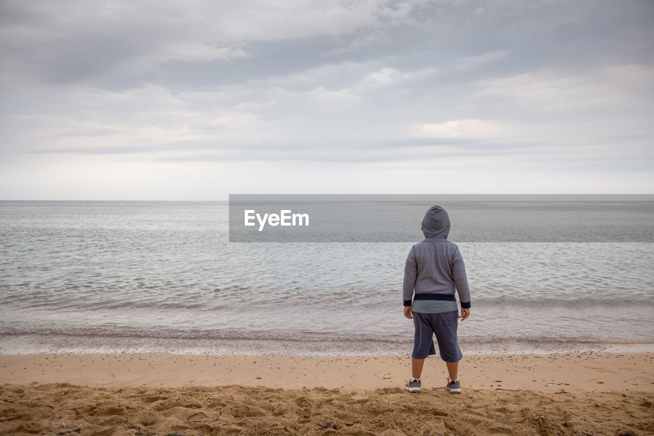 Rear view of boy standing at beach against sky