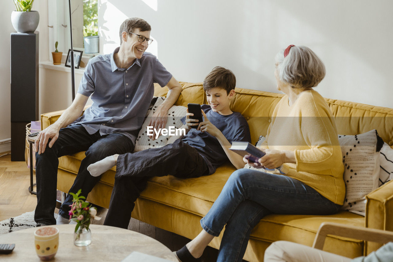 Happy man sitting on sofa with son and mother-in-law at home