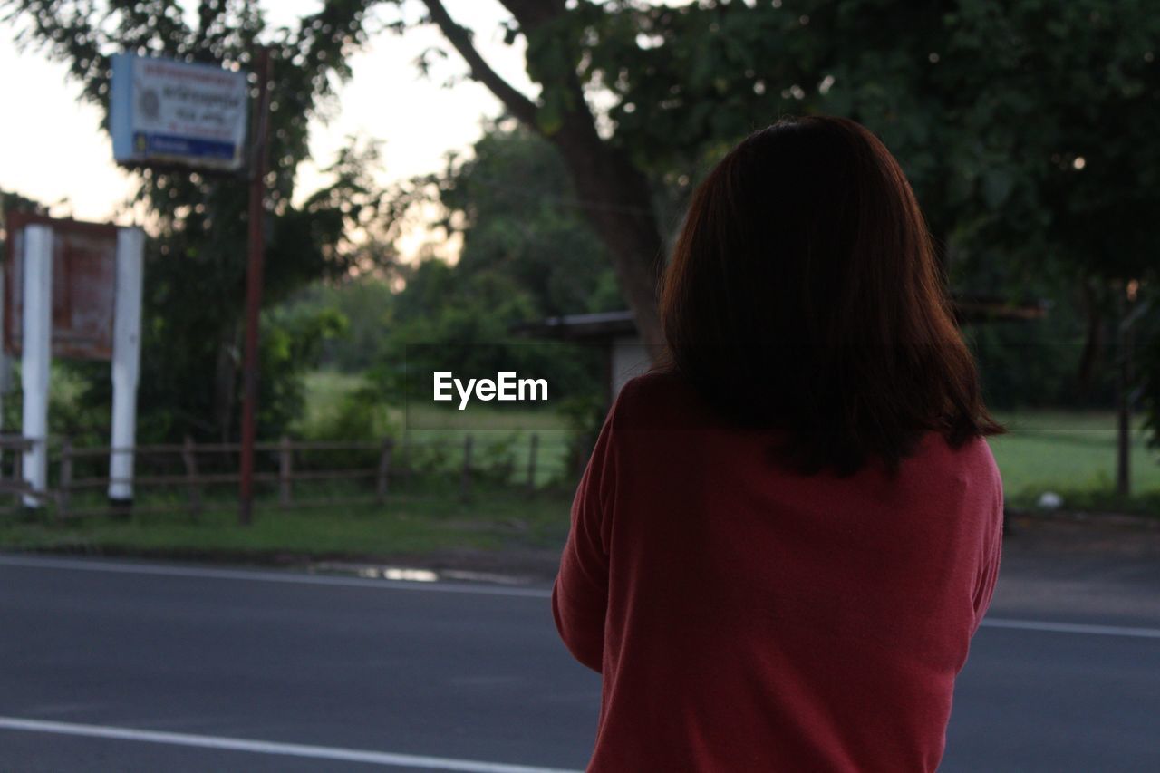 REAR VIEW OF WOMAN STANDING ON ROAD AGAINST TREES