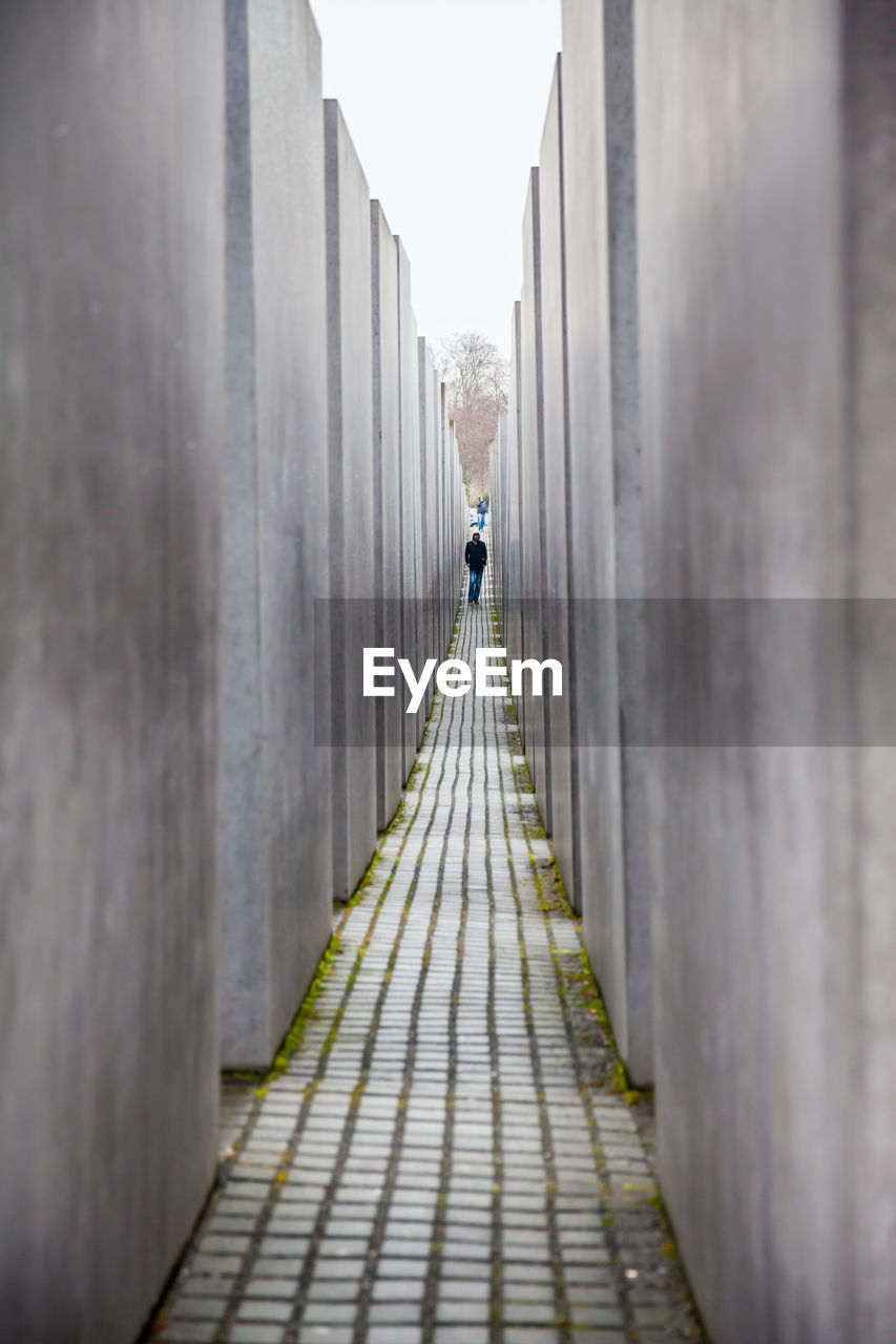 REAR VIEW OF WOMAN WALKING ON FOOTPATH AMIDST BRIDGE