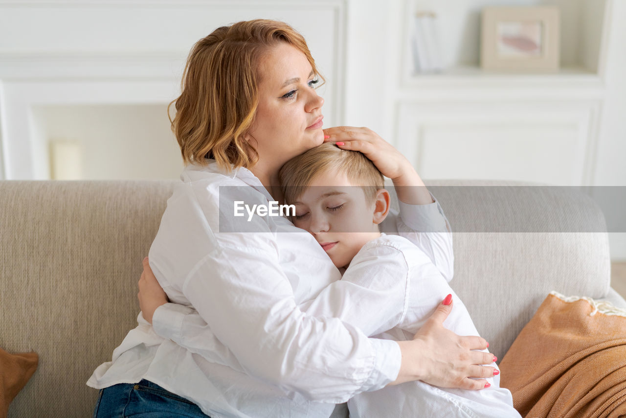 Happy young mom hugs her toddler son, relaxing on sofa at home. cute toddler