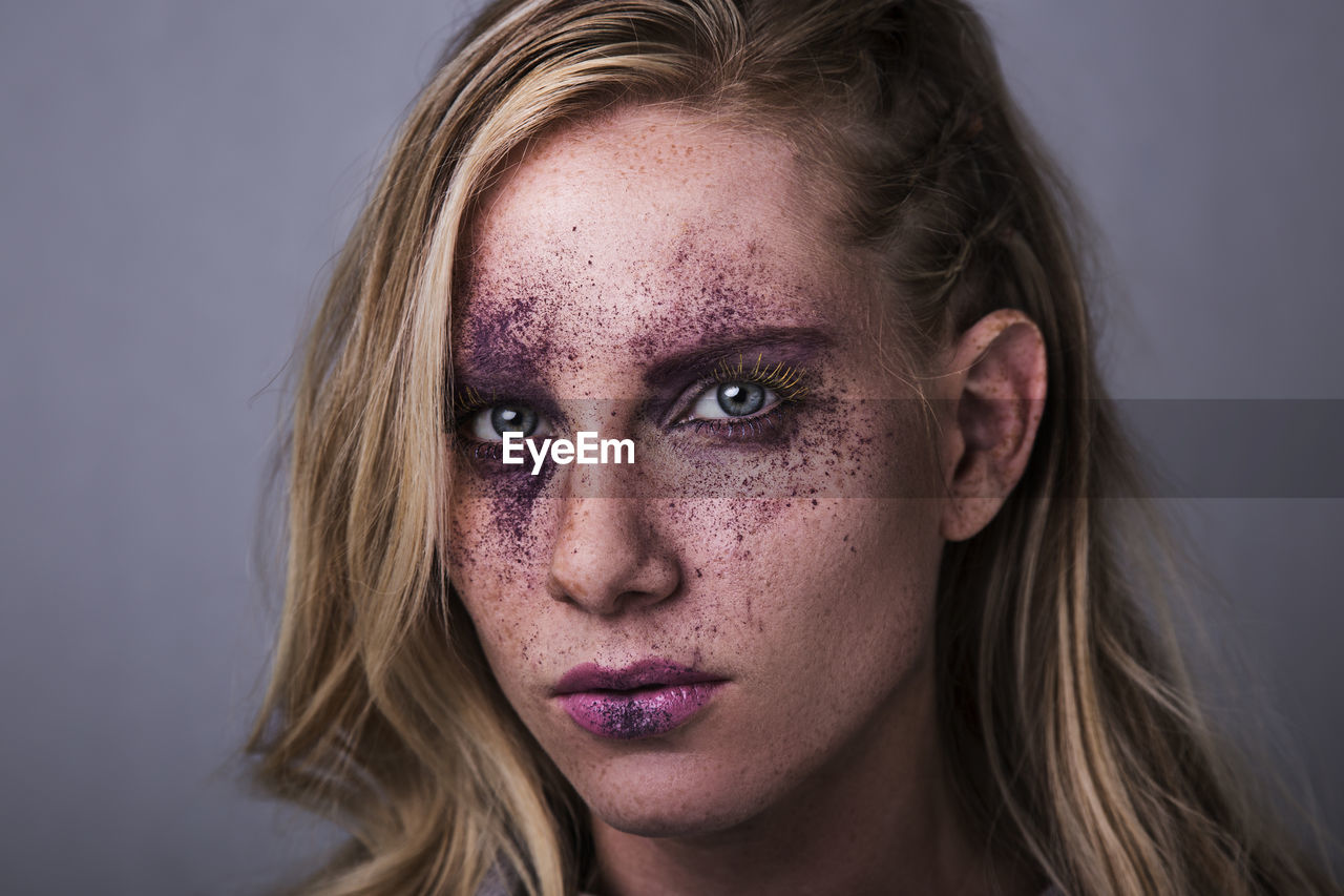 Close-up portrait of woman with purple bruise make-up against gray background