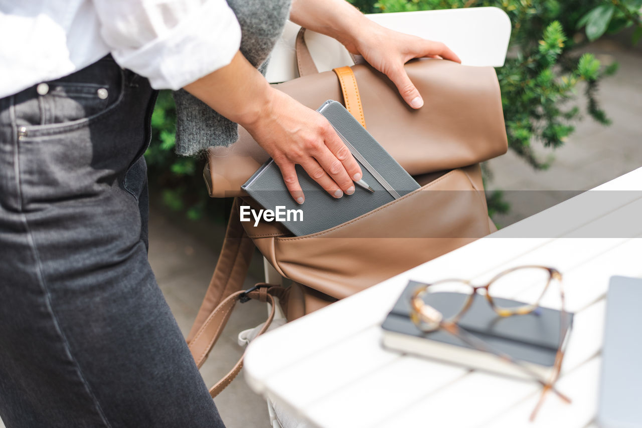 A woman in casual clothes takes out a notebook and a pen from her backpack for a work meeting.