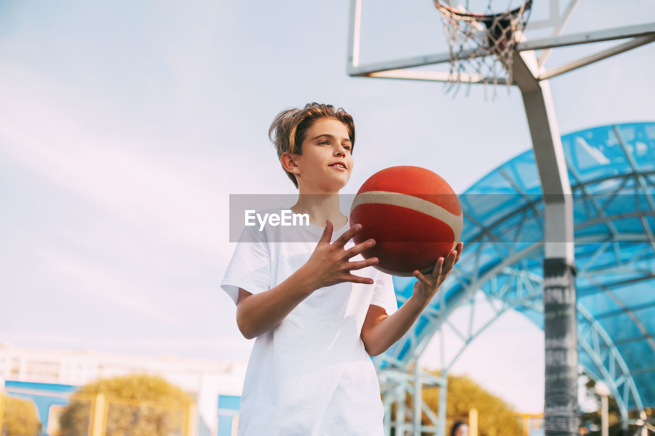 Low angle view of boy playing with basketball against sky