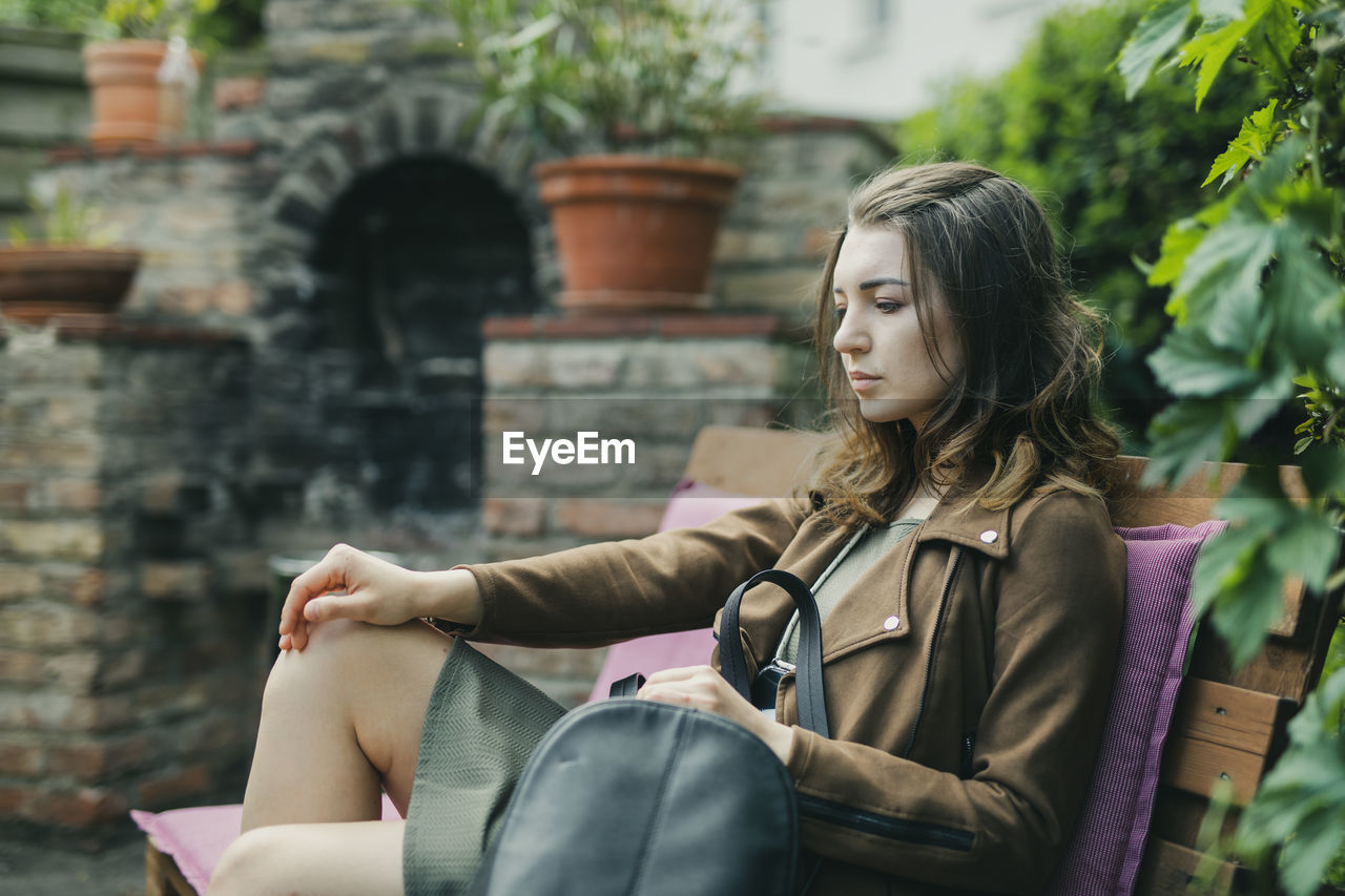 Side view of thoughtful beautiful woman sitting on bench