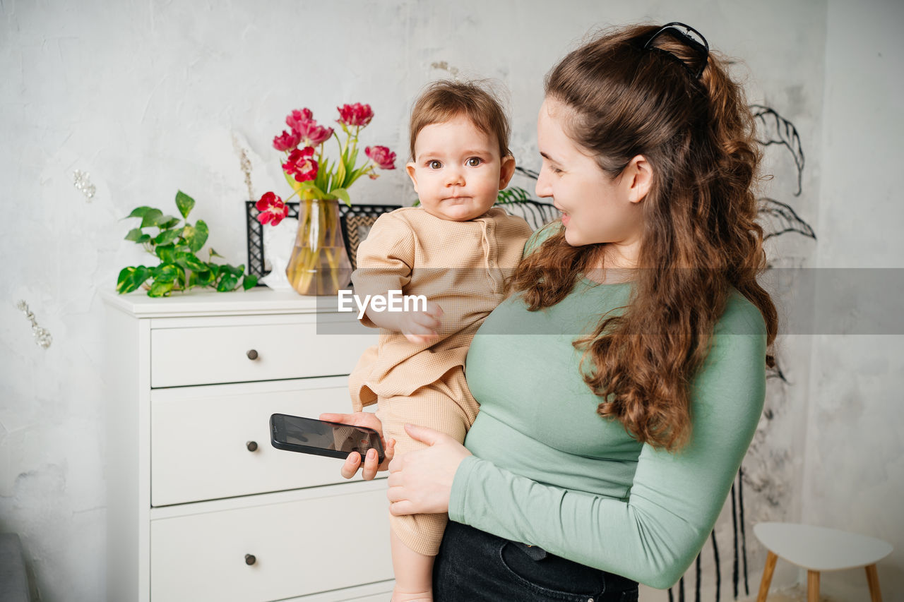 Mother with a child in her arms in a room with flowers smartphone