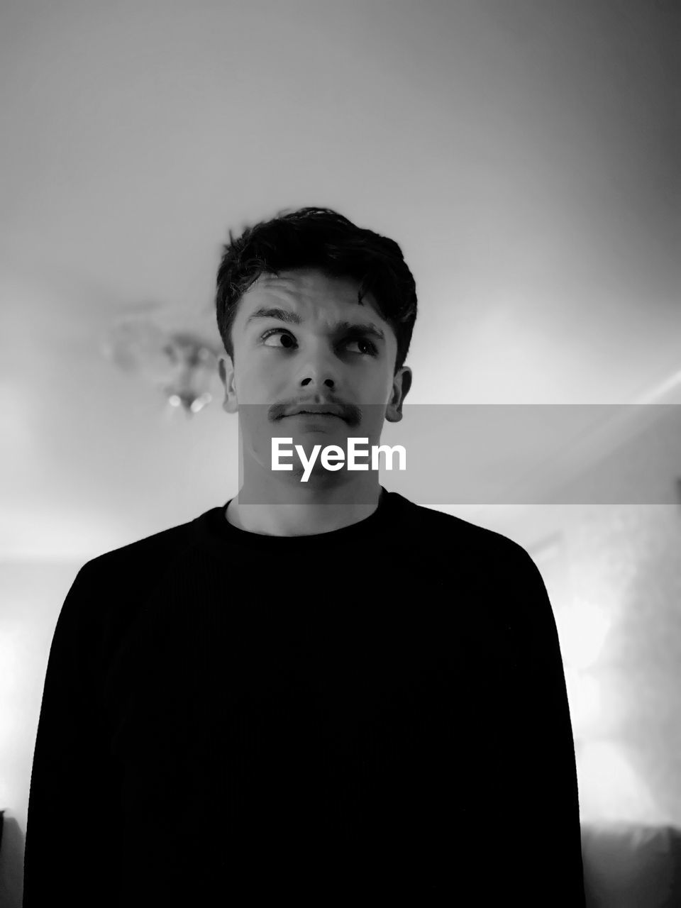 Young man looking away while standing at home