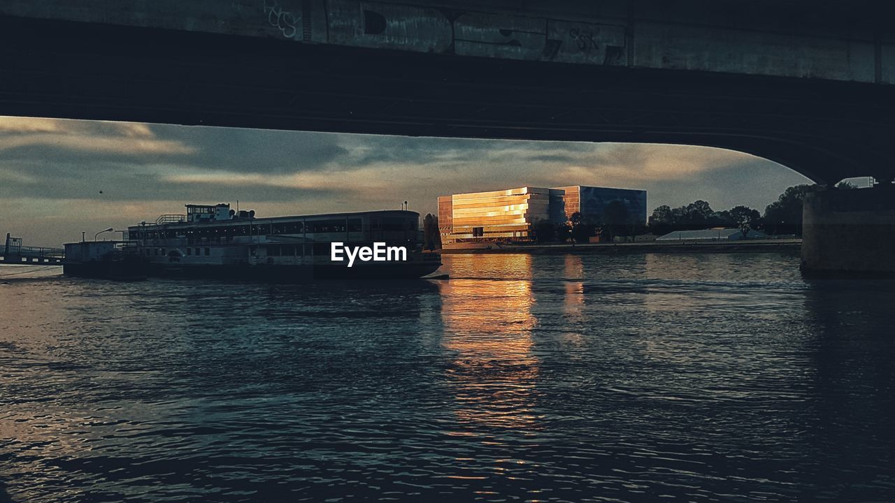 BRIDGE OVER RIVER IN CITY AGAINST SKY DURING SUNSET