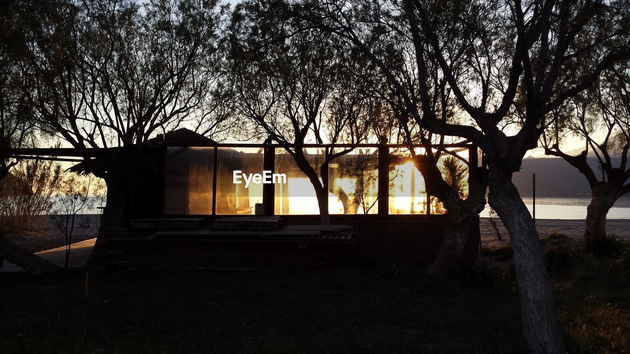 Exterior of house amidst silhouette trees at sunset