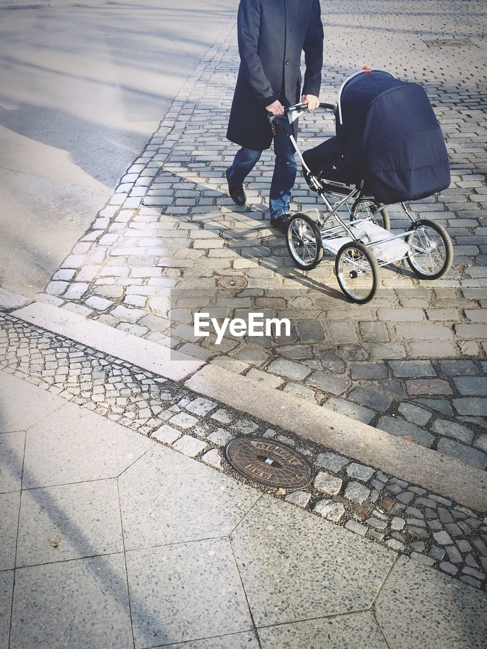 Low section of man walking with baby stroller on footpath