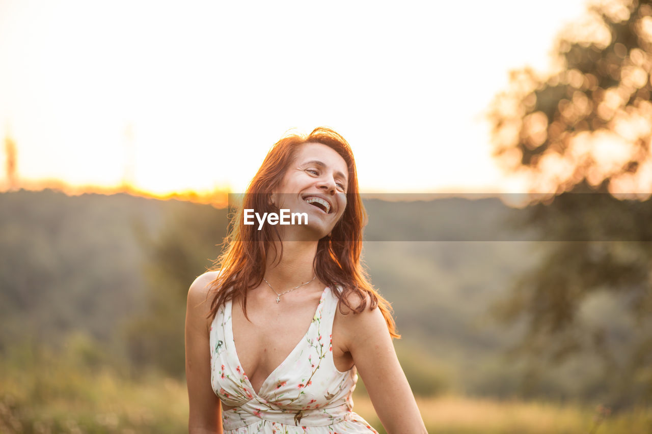 Smiling mature woman standing against sky during sunset