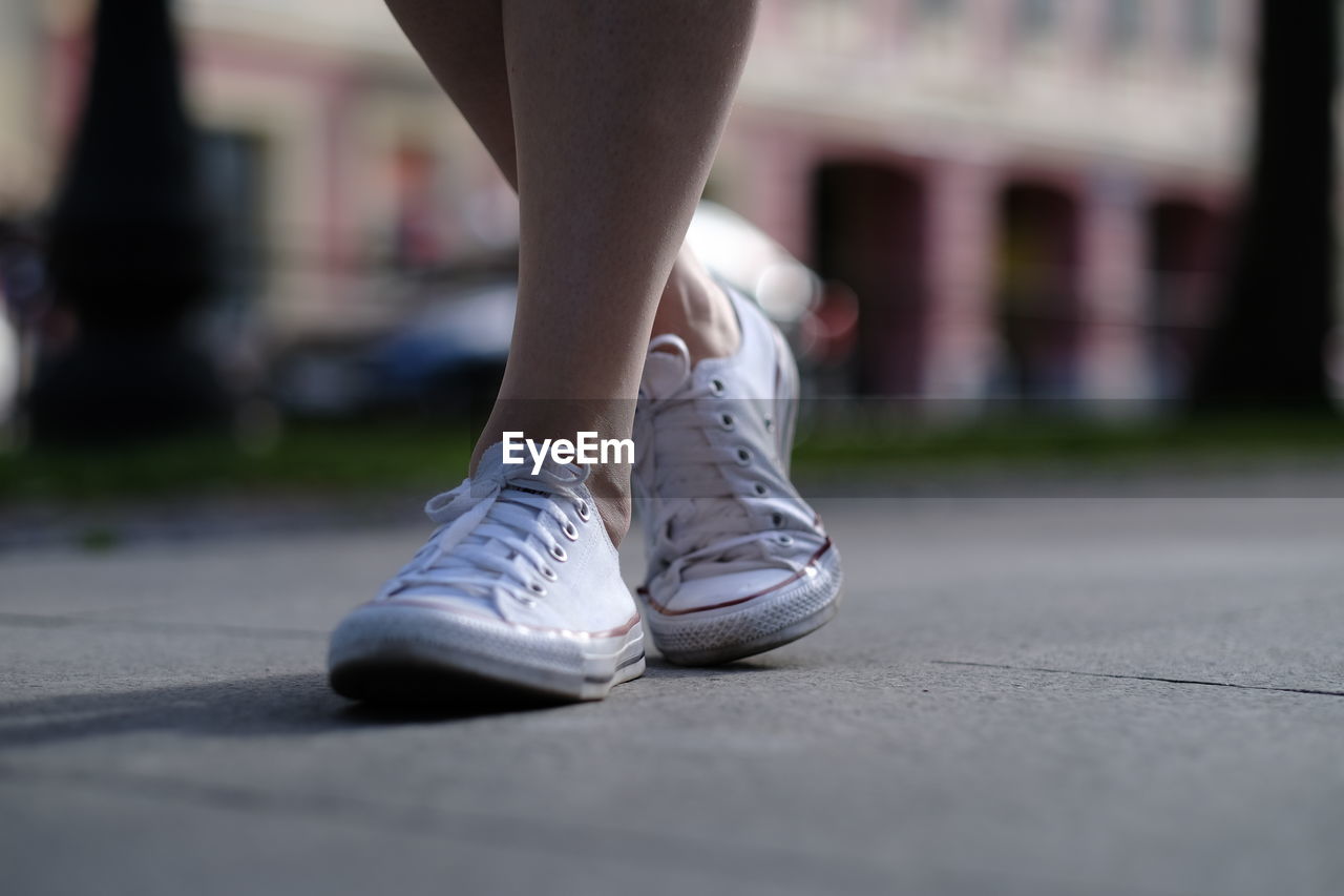 Low section of woman walking on footpath in city