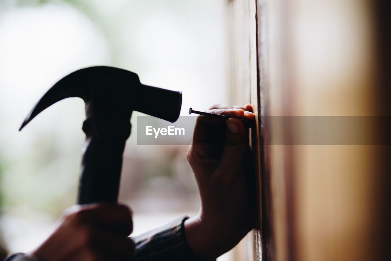 Cropped hands of person hammering nail on wall