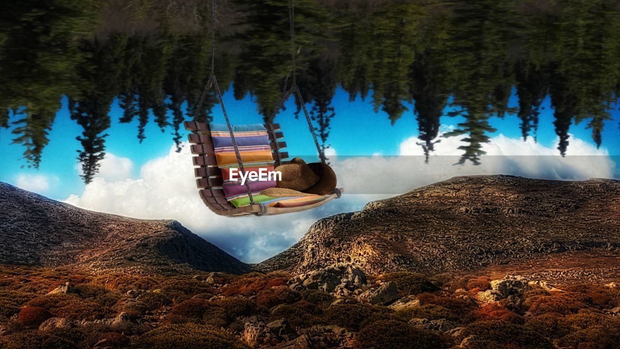 Digital composite image of swing hanging against mountains and trees