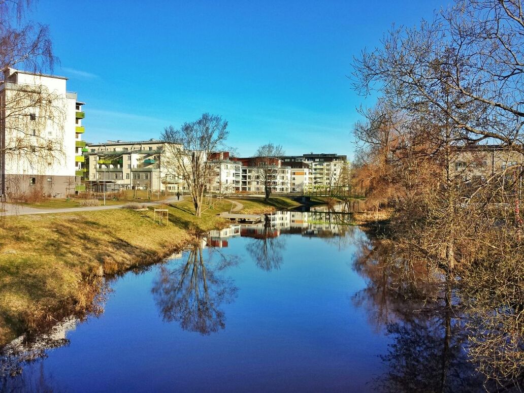 Canal leading towards houses against blue sky