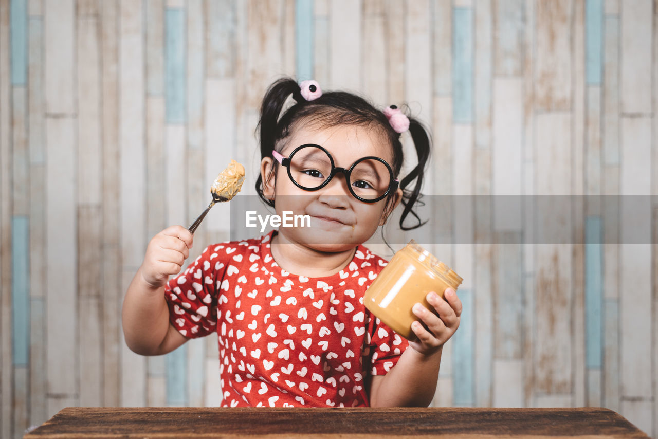 Portrait of happy girl holding spoon and peanut butter bottle