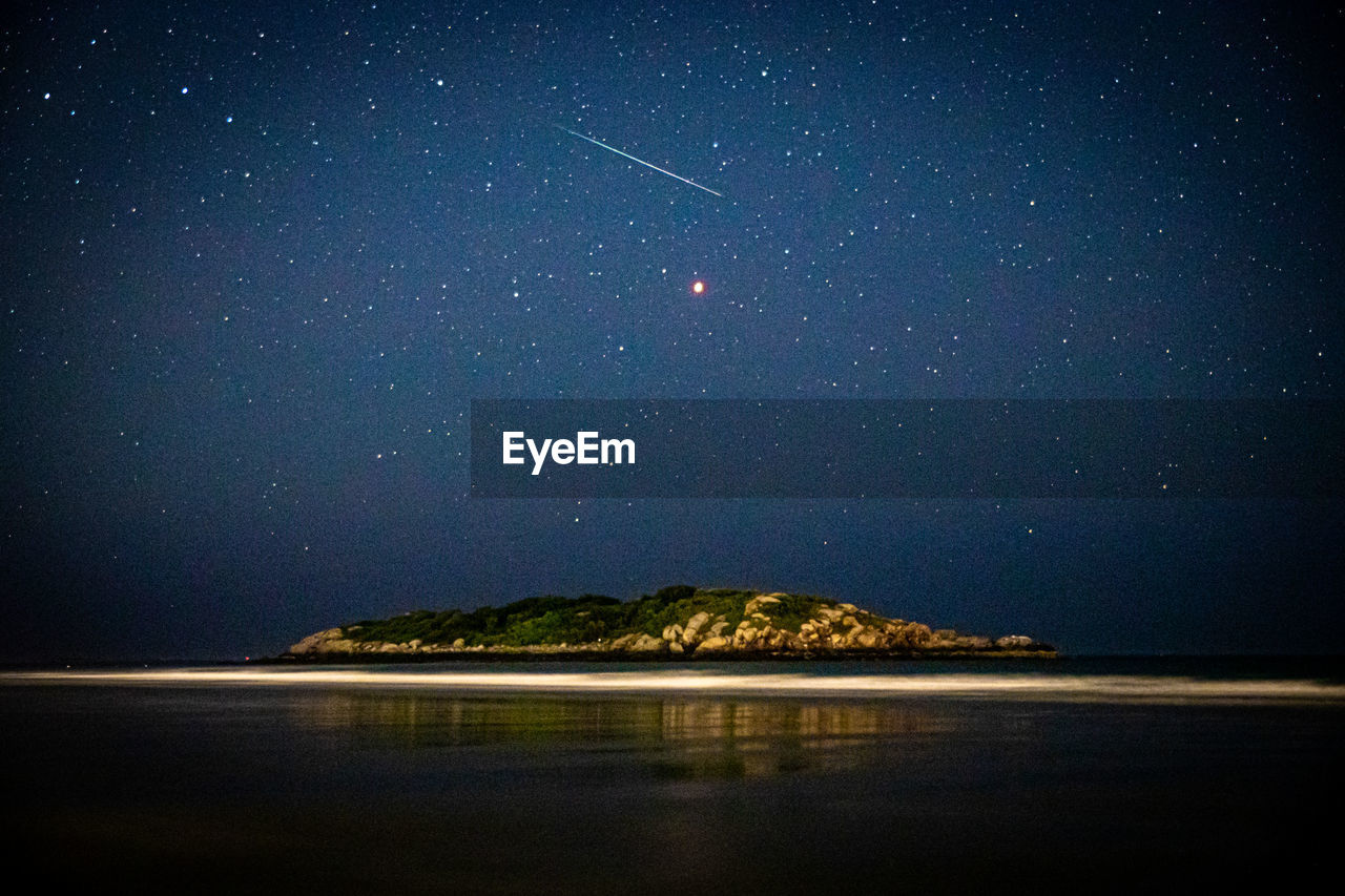 Meteor shooting through the night sky above island in ocean and mars.