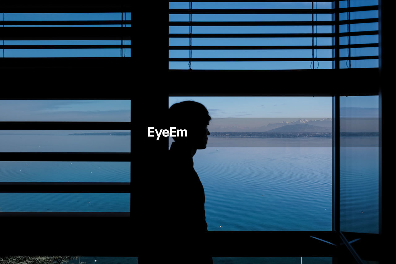 Man standing by window against lake