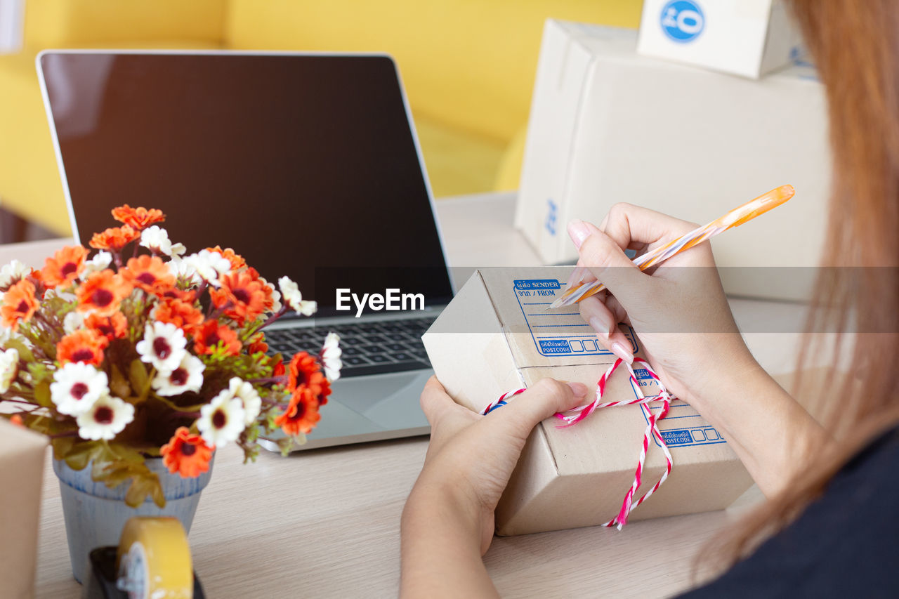 Midsection of woman using laptop while writing on box at table