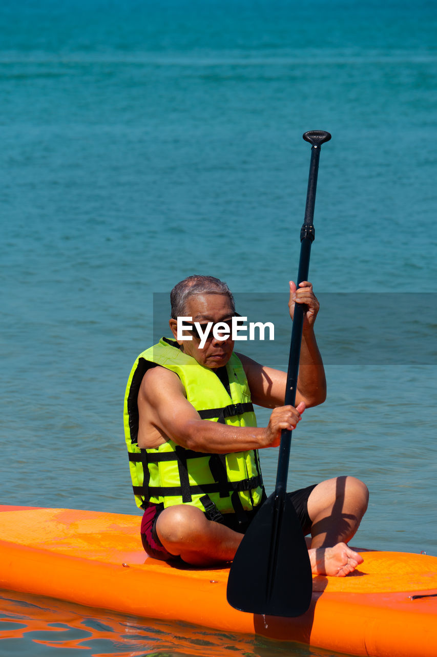 Full length of man sitting on paddleboard in sea