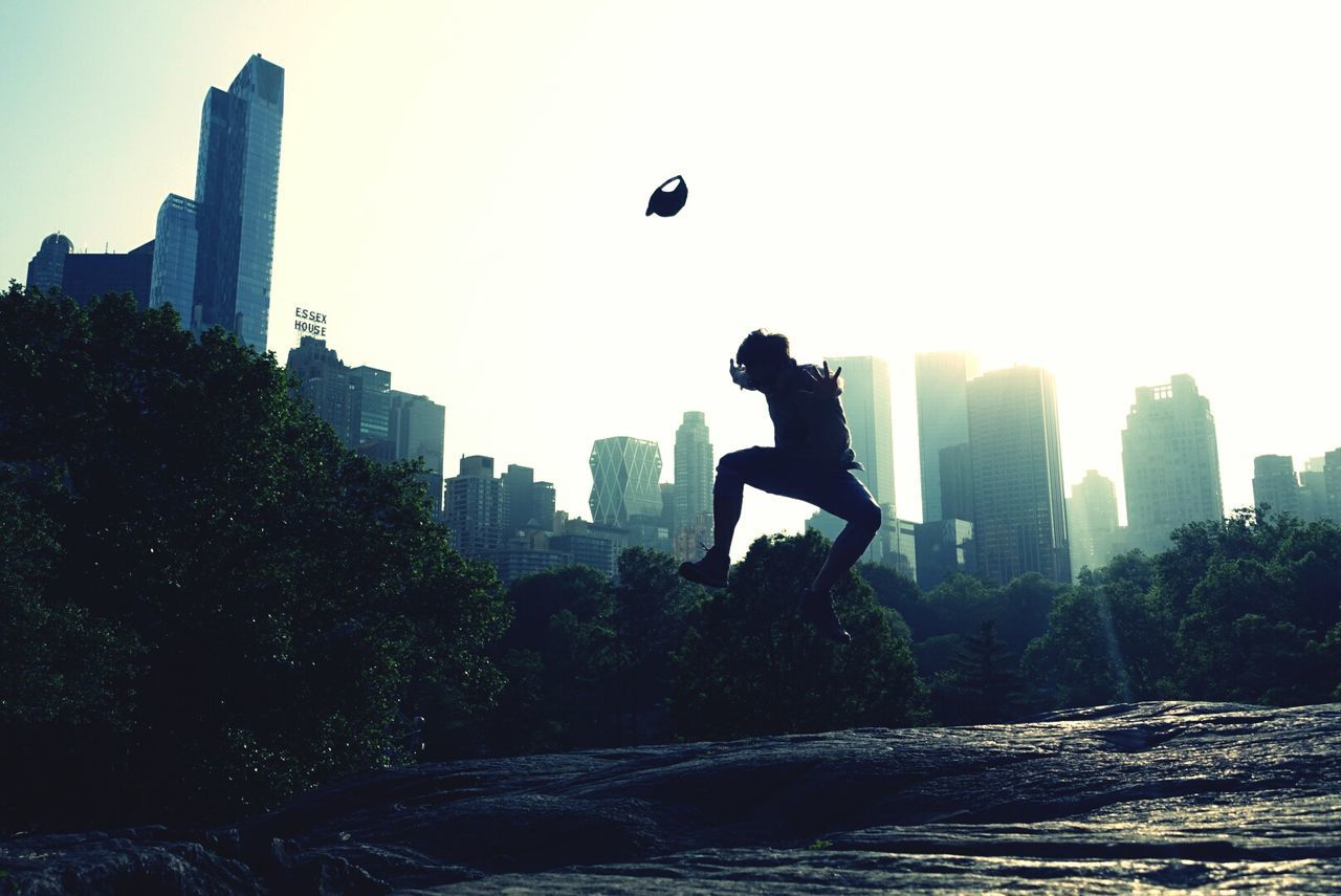 Silhouette person jumping on rock with city in background