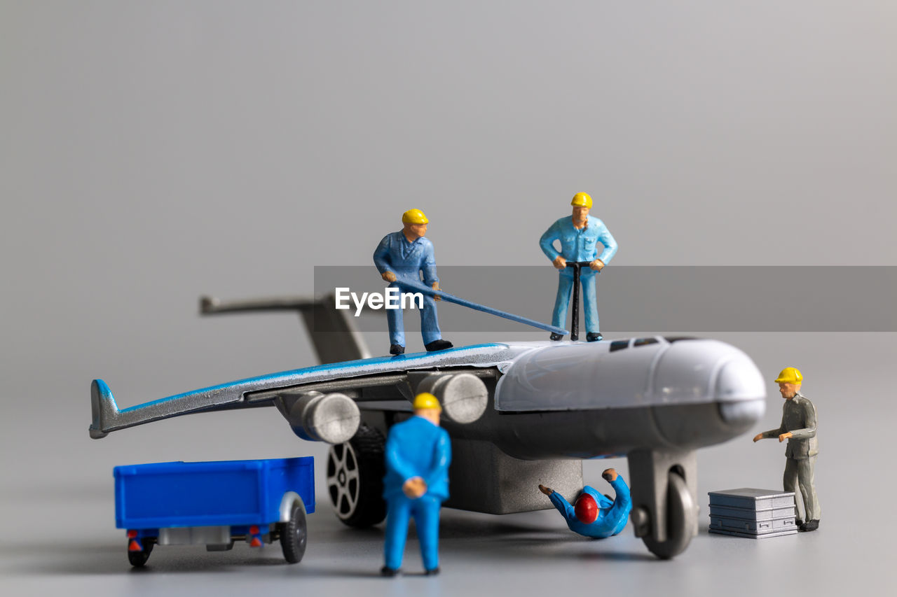 Miniature people worker team checking and repairing airplane on gray background