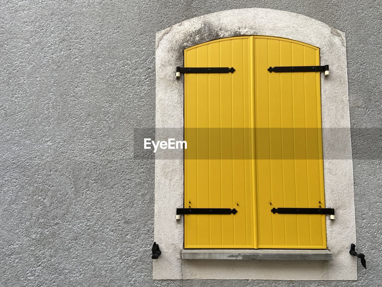 Window with closed yellow wooden shutters on the grey wall of the house