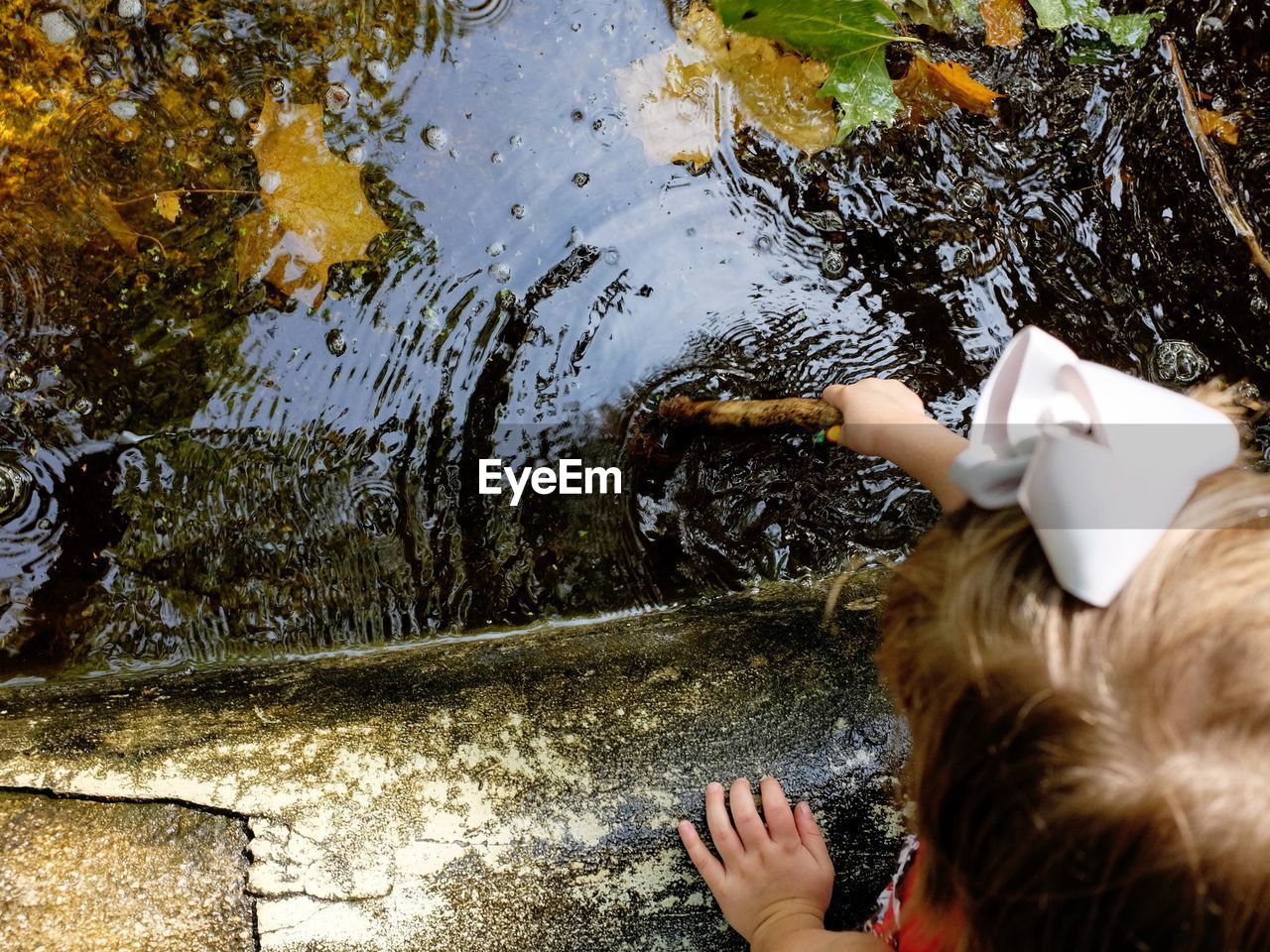 Cropped image of girl holding stick in pond at fairbury city park