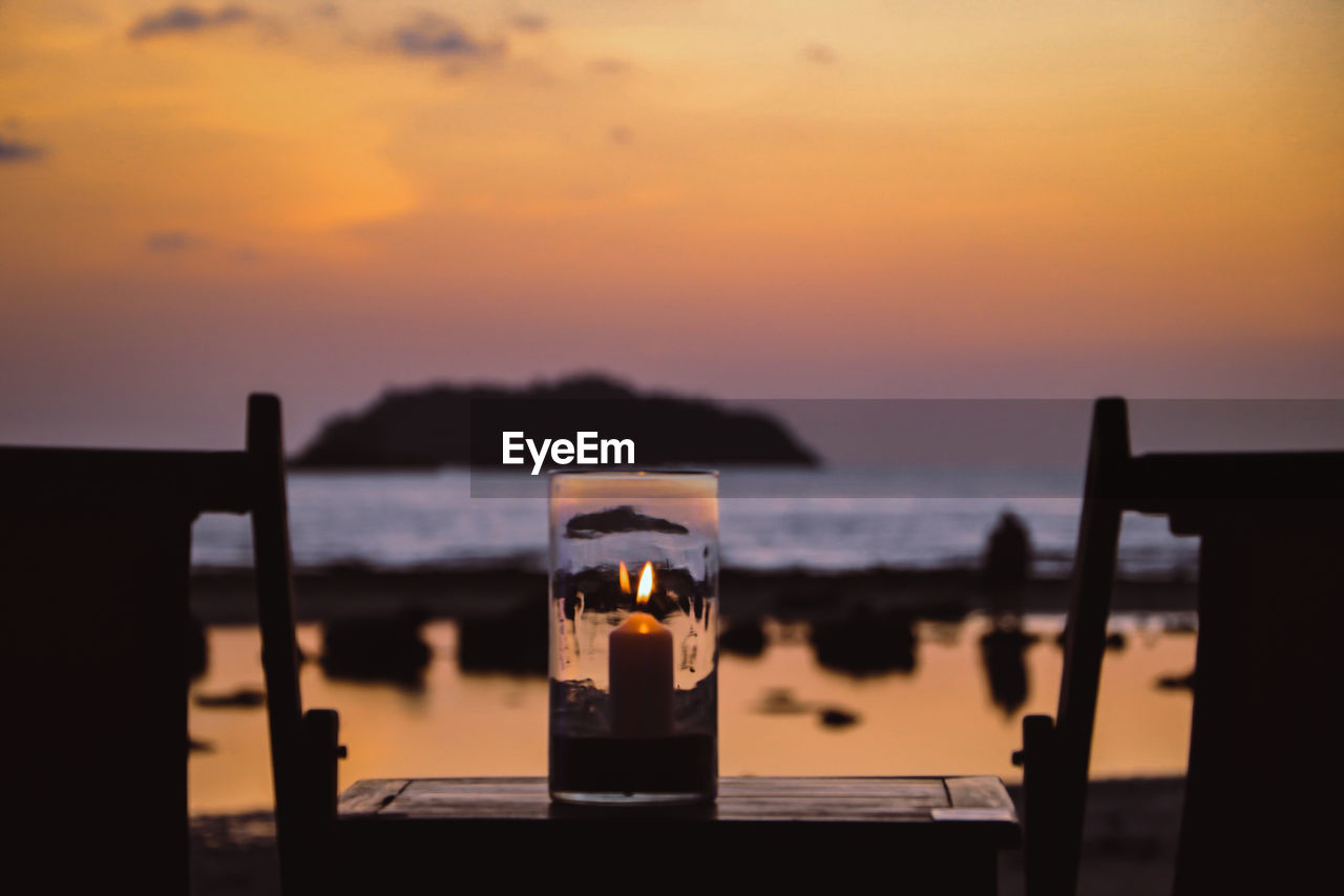 Candle on table against sea during sunset