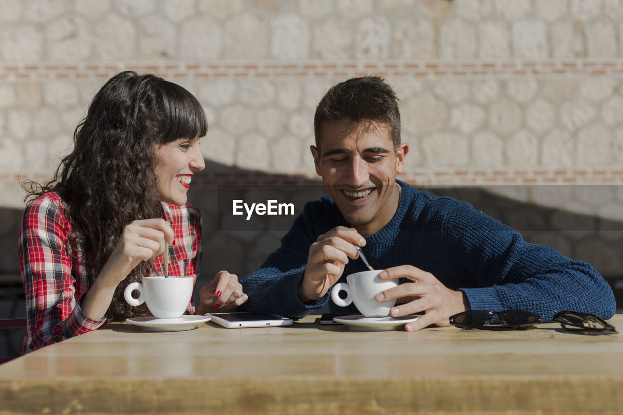 Smiling couple with coffee cups on table sitting at sidewalk cafe