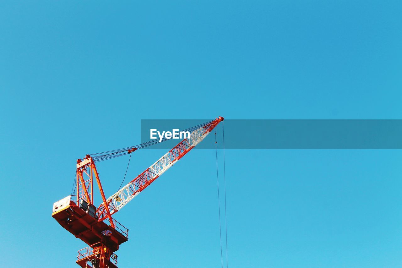 Low angle view of crane against clear blue sky