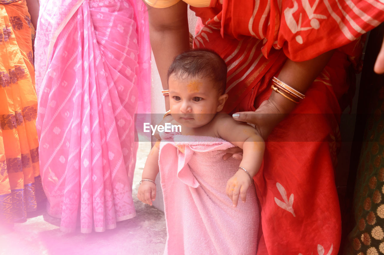 child, childhood, women, clothing, pink, female, two people, togetherness, baby, adult, innocence, person, emotion, cute, family, indoors, portrait, lifestyles, traditional clothing, positive emotion, happiness, smiling, bonding, front view, parent, dress, holding, love, event, toddler, celebration, waist up, looking, standing