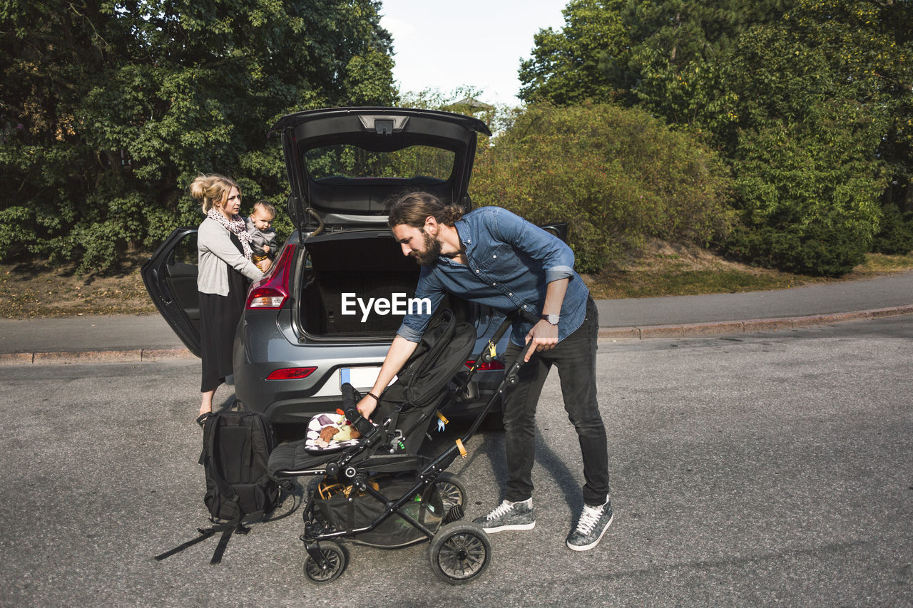 Mid adult parents with baby boy and stroller near car on street