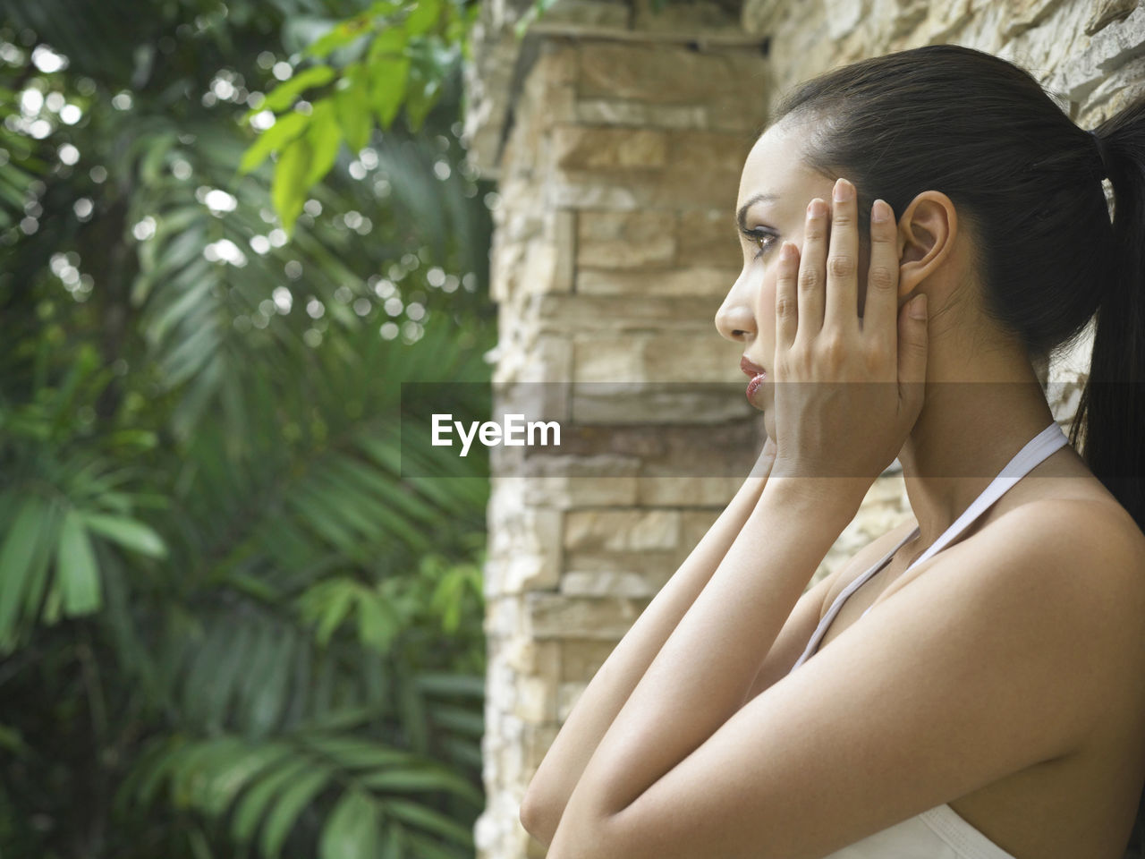 Side view of woman holding face outdoors