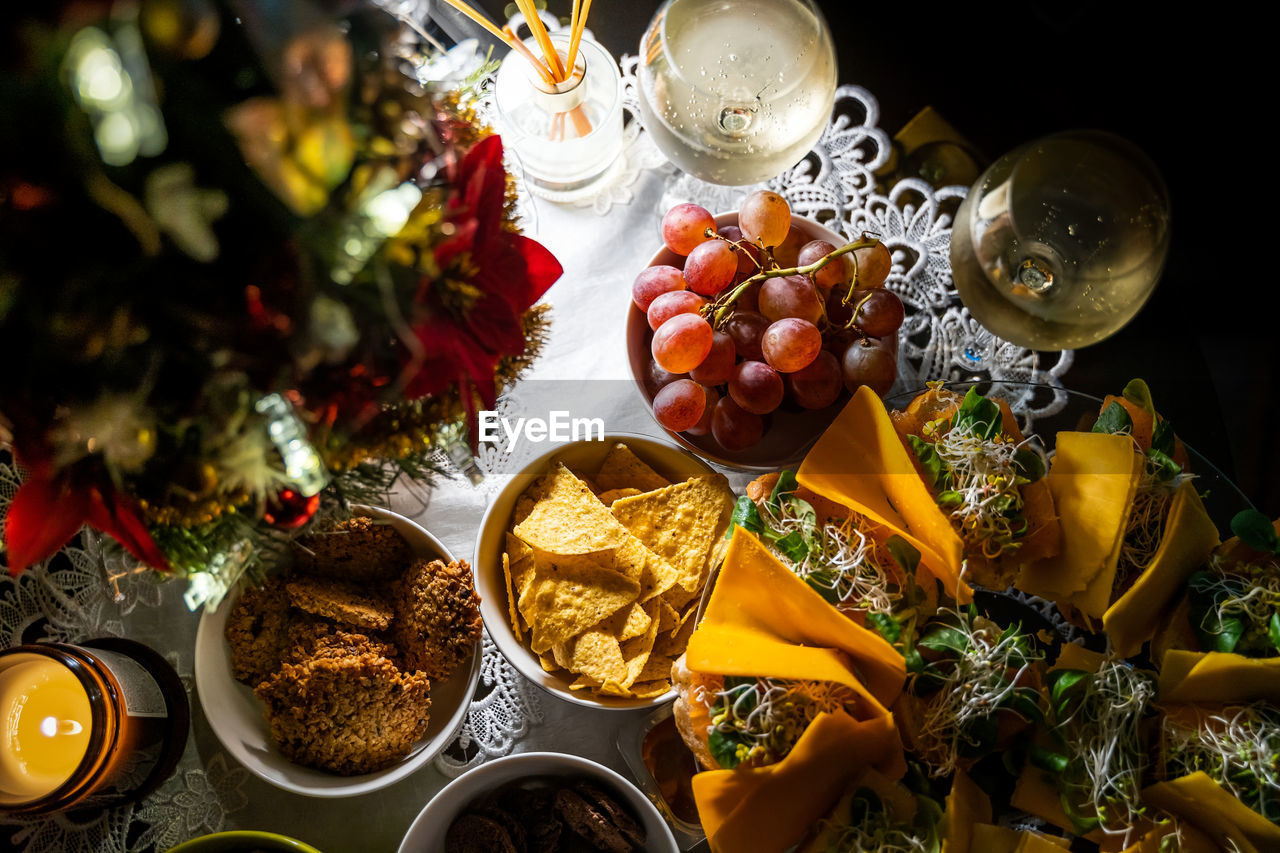 Top view of buffet snacks such as grapes, cookies, nachos, sandwiches and nuts on a table