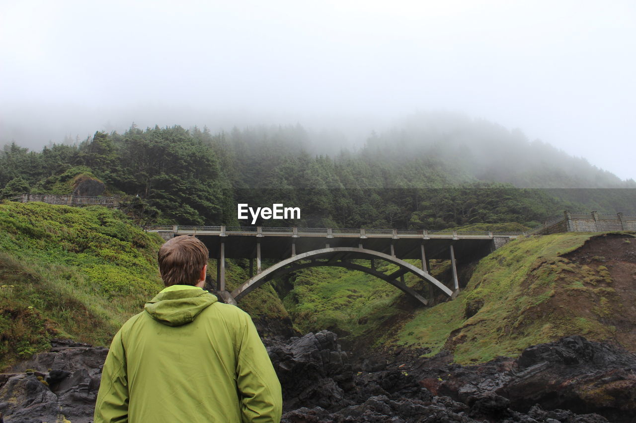REAR VIEW OF MAN ON BRIDGE AGAINST SKY