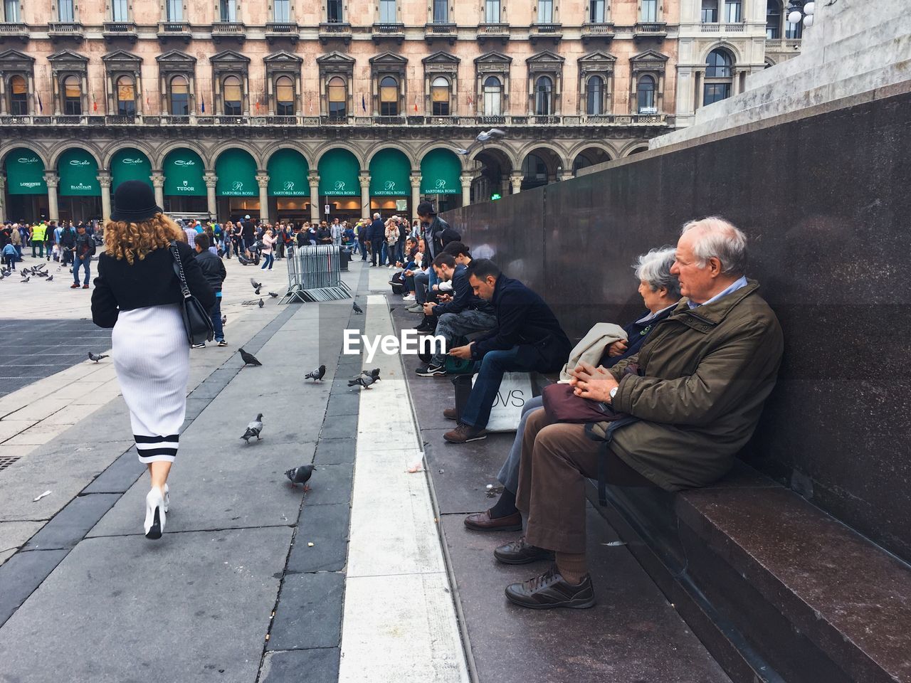 REAR VIEW OF PEOPLE SITTING IN TOWN SQUARE