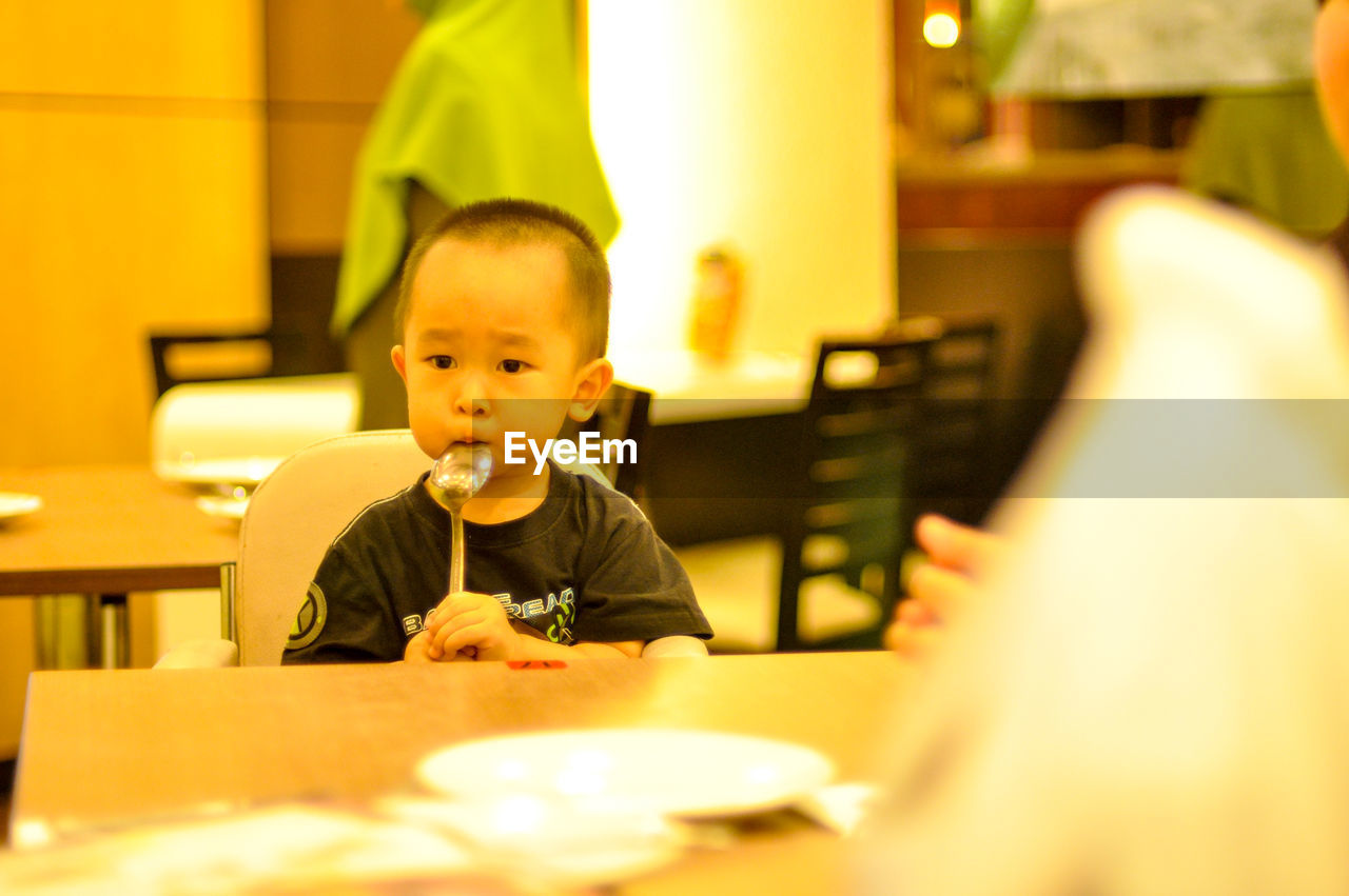 Boy holding spoon while sitting in restaurant
