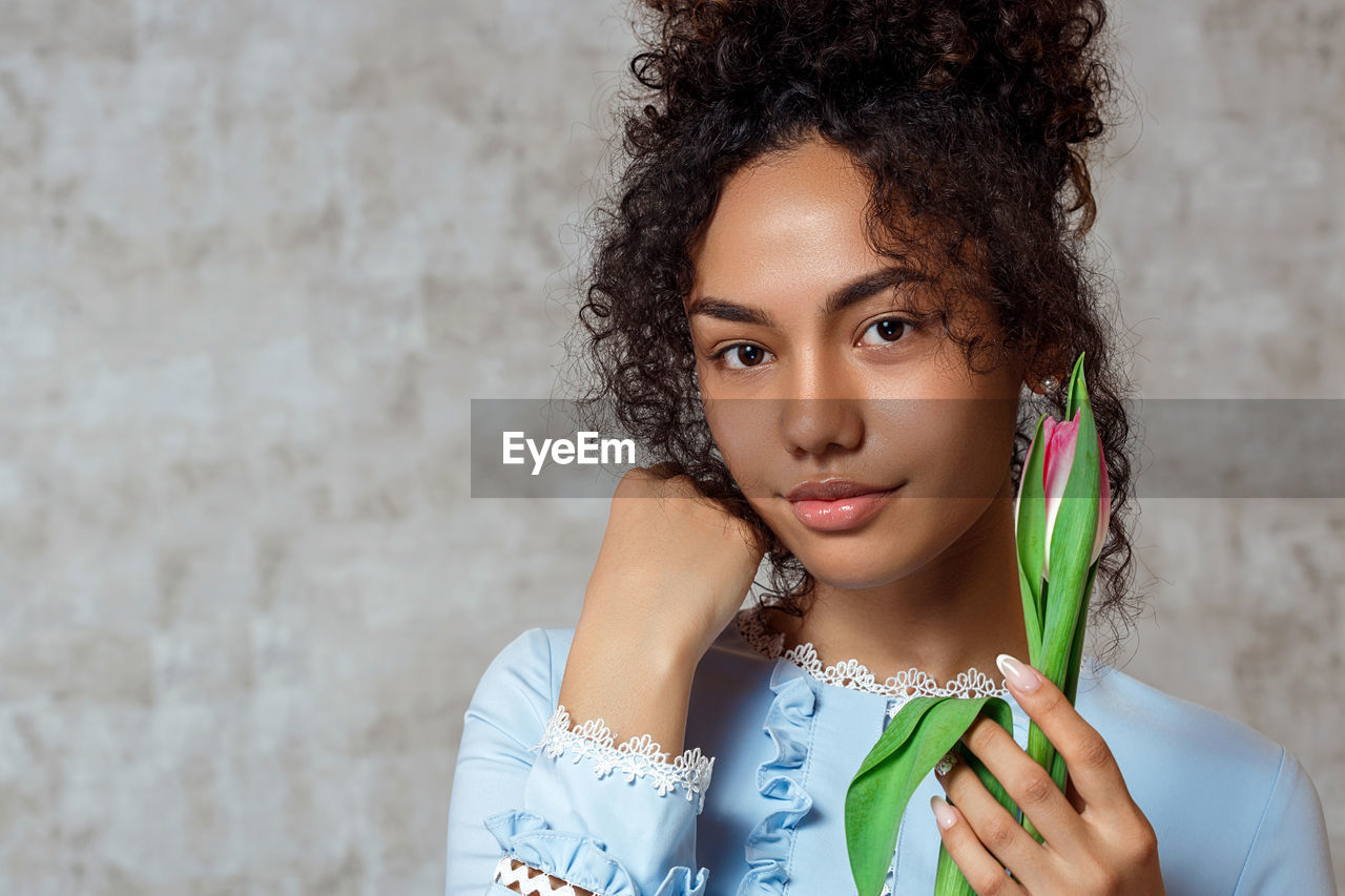 Portrait of smiling young woman holding tulip while standing against wall