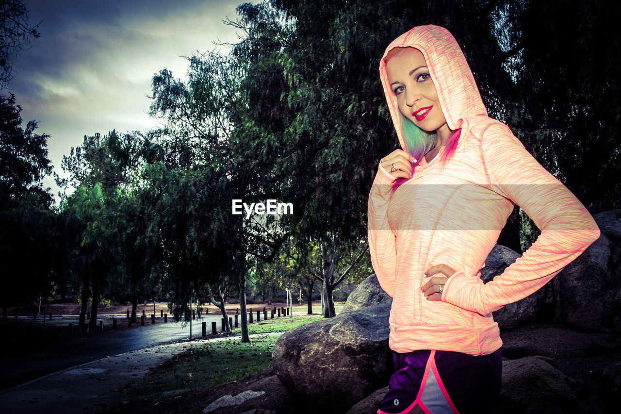 Side view portrait of young woman in hooded shirt standing at park