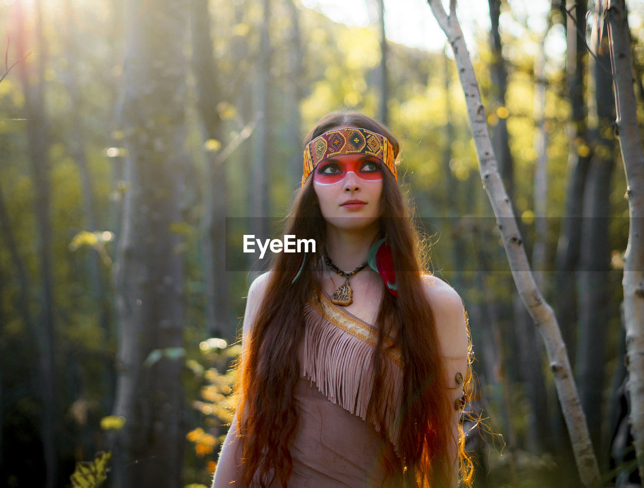 Young woman in traditional clothing looking away while standing in forest