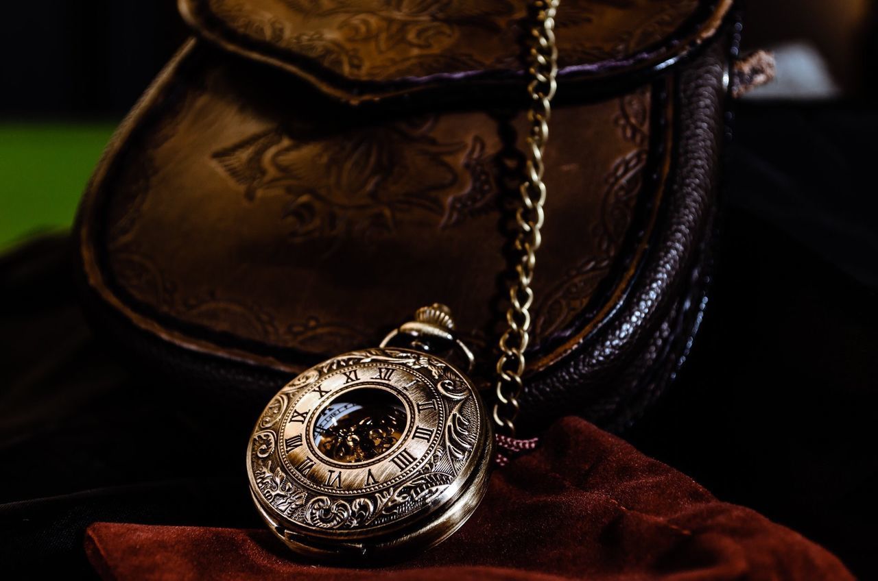 Close-up of pocket watch and bag against black background
