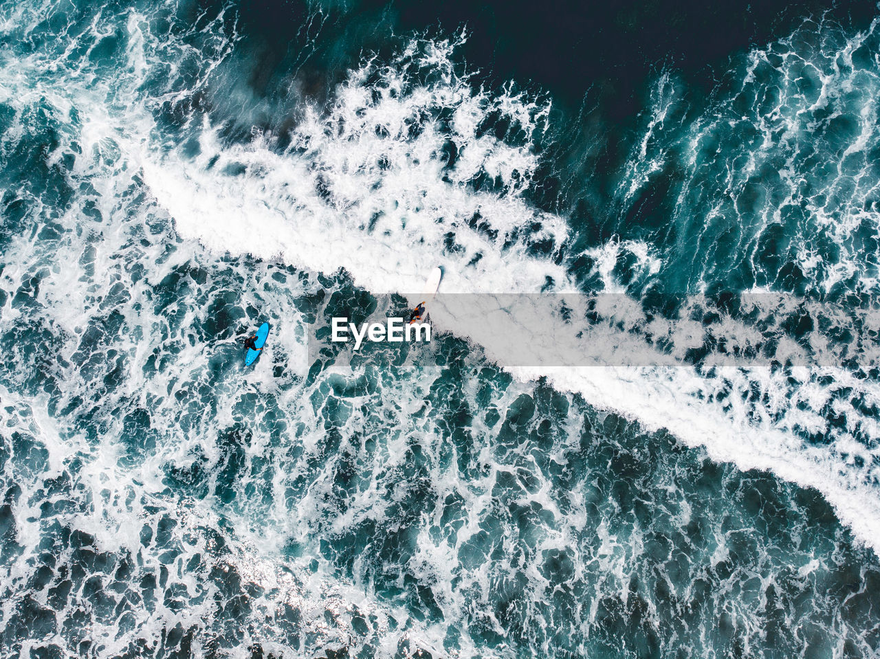 Aerial drone view over surfers with blue water and white waves in portugal.